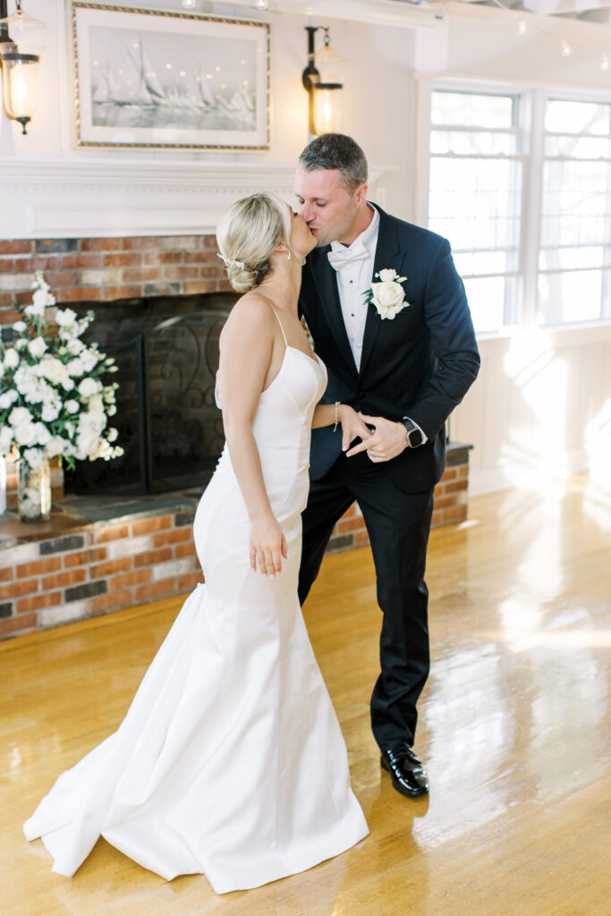 Bride and groom share a romantic kiss in front of a cozy fireplace, showing Monroe CT bridal makeup and hair artistry